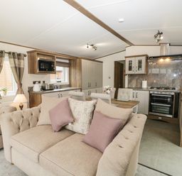A living area with beige sofas and pillows next to a kitchen with wooden cabinets and appliances at Ashton Lodge - Sherwood 4 in South Lakeland Leisure Village