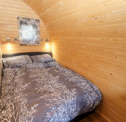 A bedroom with a double bed and wooden paneled walls at Goose Pod Near Clifton Upon Teme