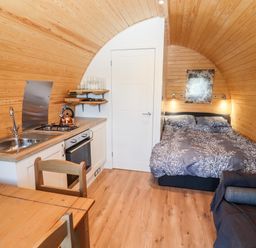 A small wooden room with a kitchen area dining table bed and sofa at Gander Pod Near Clifton Upon Teme