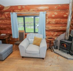 A living room with a sofa, armchair, and stove at Cedar Cabin at Salford Court Farm Fishing Cabins near Clifton Upon Teme