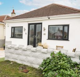 A small white house with black window frames and doors behind a low stone wall with plants in front at Cove House in Kinmel Bay