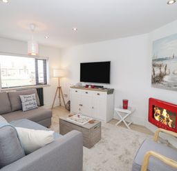 A living room with grey sofas a wooden chest coffee table a red fireplace and a TV on a white cabinet at Cove House in Kinmel Bay