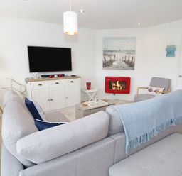 A living room with a gray sofa and blue throw blanket a wall-mounted television and a red fireplace at Cove House in Kinmel Bay