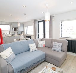 An open plan living room and kitchen with a grey sofa, round dining table, red refrigerator and large windows at Cove House in Kinmel Bay