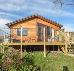 A wooden cabin with a raised deck and chairs in a grassy area at Oaks One Swarland near Felton