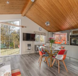 A kitchen and dining area with a glass table set for four and a wall-mounted TV with a door opening to an outdoor deck at Oaks One Swarland near Felton