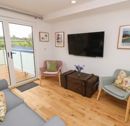 A living room with a gray sofa and two armchairs facing a wall-mounted TV and a wooden chest at Pinot in Seaview
