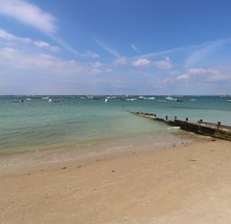 A sandy beach with a wooden jetty and boats floating on the water at Pinot in Seaview
