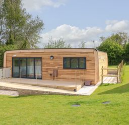 A wooden cabin with glass sliding doors and a deck surrounded by grass and trees at Pinot in Seaview