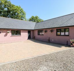 A courtyard with pink exterior walls black-framed windows hanging flower pots and a tiled driveway at 1 The Warren Robeston Wathen near Narberth