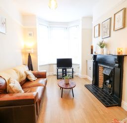A living room with a brown leather sofa a wooden coffee table a small television on a stand and a black fireplace at Number 91 in Belfast County Antrim