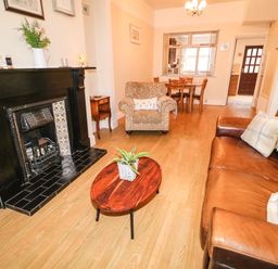 A living room with a leather sofa, armchair, wooden coffee table with a plant, black fireplace and dining table at Number 91 in Belfast County Antrim