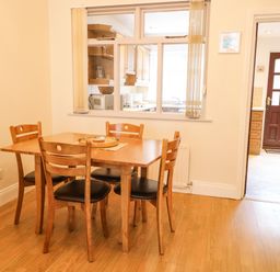 A dining area with a wooden table and four chairs next to a window opening to a kitchen at Number 91 in Belfast County Antrim