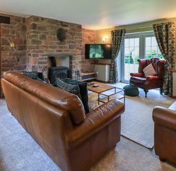 A living room with leather sofas a stone fireplace a red armchair and a wall mounted TV at Flaska House in Troutbeck Near Penrith