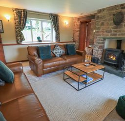 A living room with two brown leather sofas a wood burning stove and a wooden coffee table at Flaska House Troutbeck Near Penrith