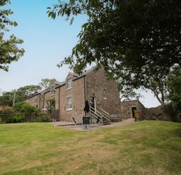A stone house with a lawn and patio furniture surrounded by trees at 1 Roddam Rigg Cottage in Roddam near Wooler