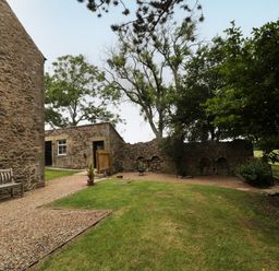 An outdoor area with stone buildings a wooden bench gravel paths grass and trees at 1 Roddam Rigg Cottage in Roddam near Wooler