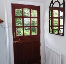 An interior hallway with a wooden door with glass panels a wall mirror and a radiator at 1 Roddam Rigg Cottage Roddam near Wooler