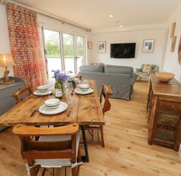 A dining area with a wooden table set for four next to a living room with a sofa and wall-mounted TV at Syrah in Seaview
