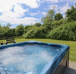 An outdoor hot tub with bubbling water on a patio next to a grassy garden with chairs and trees at Syrah in Seaview