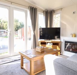A living room with a wooden coffee table a grey sofa a television on a wooden stand and a fireplace at Hawthorn Lodge in South Lakeland Leisure Village