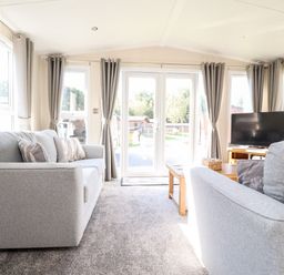 A living room with two grey sofas a wooden coffee table a television and large windows with grey curtains at Hawthorn Lodge in South Lakeland Leisure Village