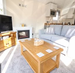 A living room with a wooden coffee table a grey sofa a TV on a wooden stand and a fireplace at Hawthorn Lodge South Lakeland Leisure Village