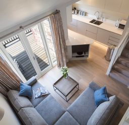 A living room with a sectional sofa and a coffee table next to a kitchen and stairs at 5 Keeper's Cottage Hillfield in Dartmouth