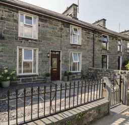 A stone house with white framed windows and a dark brown front door with a small fenced patio at Minffordd in Trawsfynydd
