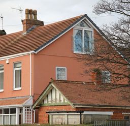 A two-story house with orange walls and a red tiled roof with chimneys and windows and a bare tree in front at The Headlands - Gower in The Mumbles