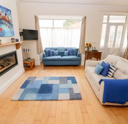 A living room with two sofas a blue rug a fireplace and a wall-mounted TV at The Headlands - Gower in The Mumbles
