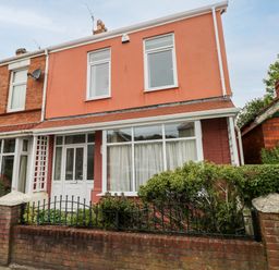 A two story house with pink and red exterior walls and a garden behind a brick wall and black metal fence at The Headlands - Gower in The Mumbles