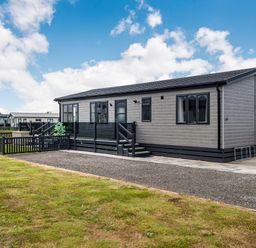 A single-story modular home with a fenced yard and steps leading to a glass-panelled porch at Number 8 Lakes View in Brean