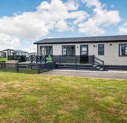 An external view of a single-story modern mobile home with a fenced yard at Number 8 Lakes View in Brean