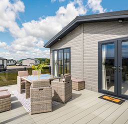 An outdoor patio with a dining table and chairs beside a modern cabin at Number 8 Lakes View in Brean