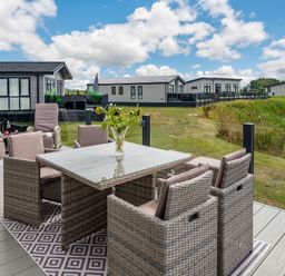 An outdoor patio with wicker chairs and a table with flowers near a lake at Number 8 Lakes View in Brean