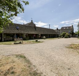 A courtyard with a gravel driveway benches and potted plants outside stone cottages at Tinkley Cottage in Nympsfield near Nailsworth