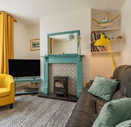 A living room with a teal fireplace black stove yellow armchair and black sofa with green cushions at Sea Spray in Watchet
