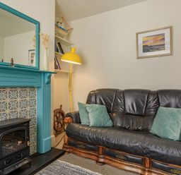 A living room with a black leather sofa green cushions a yellow floor lamp blue mantelpiece with a mirror and a wall painting at Sea Spray in Watchet