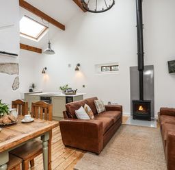 A living room with two brown leather sofas a fireplace a wooden dining table with chairs and a small kitchen area at Yr Hen Oriel in Llanrug
