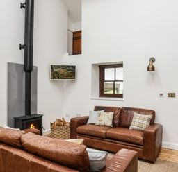 A living room with two brown leather sofas a wood-burning stove and a wooden door at Yr Hen Oriel in Llanrug