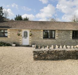 A stone cottage with a white door and three windows a stone wall and gravel driveway outside at Orchard House Cottage in Malmesbury