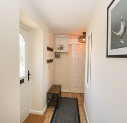 A hallway with a white door a wooden bench coat hooks a hanging light and a bird picture on the wall at Orchard House Cottage in Malmesbury