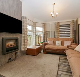 A living room with two sofas a television above a fireplace and windows with curtains at Wansfell View Limefitt Park near Troutbeck