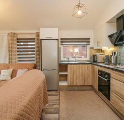 A kitchen with wooden cabinets a refrigerator an oven and a sink next to a living area with a sofa at Wansfell View in Limefitt Park near Troutbeck