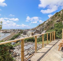 A hillside view with railing and wooden bench overlooking buildings and the sea at Windycroft in Barmouth