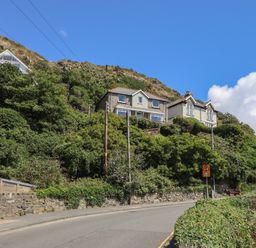 A road with houses on a hillside covered with greenery and a stone wall at Windycroft in Barmouth