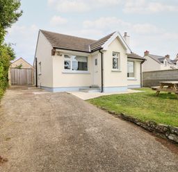 A single story house with a driveway, green lawn, and picnic table at Chalfonts Cottage in Trefin near Penparc