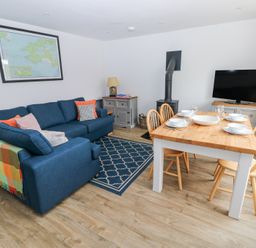A living room with a blue sofa a wooden dining table set for four a TV on a stand a wood stove and a framed map on the wall at Chalfonts Cottage in Trefin near Penparc