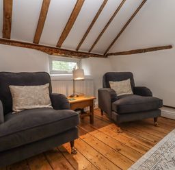 A room with two armchairs separated by a wooden side table with a lamp on a wooden floor with exposed ceiling beams at 1 White House Cottages Bromsash near Lea